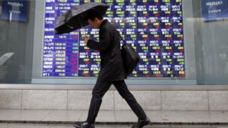 Asian-stocks - man walking in the rain in front of live rates board