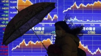 A pedestrian holding an umbrella walks past an electronic board showing the graph of the recent fluctuations of Japan's Nikkei average outside a brokerage in Tokyo February 14, 2014. REUTERS/Yuya Shino