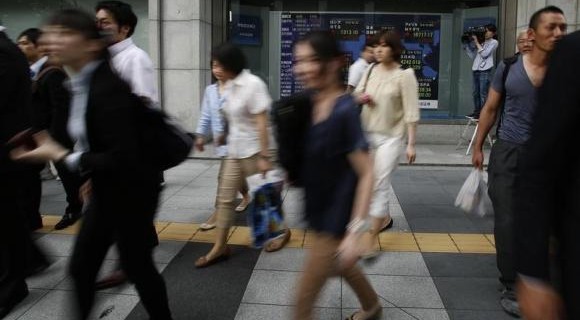 Pedestrians walk past at an electronic board outside a brokerage in Tokyo