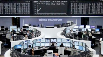 Traders are pictured at their desks in front of the DAX board at the Frankfurt stock exchange