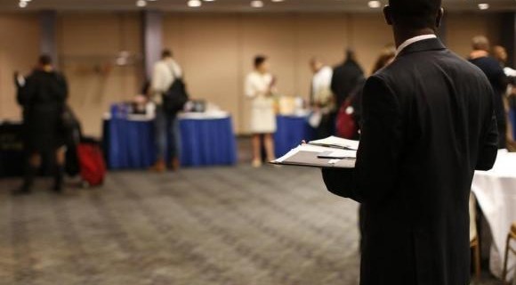 job seeker stands in a room of prospective employers at a career fair in New York City