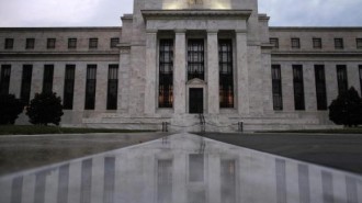 The facade of the U.S. Federal Reserve building is reflected on wet marble during the early morning hours in Washington
