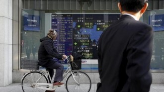 A man riding on a bicycle looks at an electronic board showing the stock market indices of various countries outside a brokerage in Tokyo