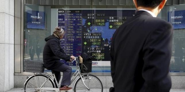 A man riding on a bicycle looks at an electronic board showing the stock market indices of various countries outside a brokerage in Tokyo