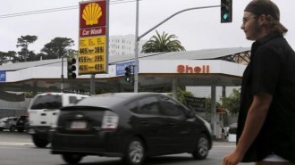 A pedestrian stands near a sign displaying the cost of gasoline at a filling station in San Francisco