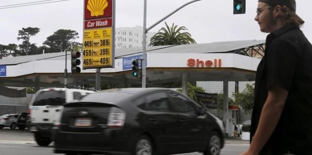 A pedestrian stands near a sign displaying the cost of gasoline at a filling station in San Francisco