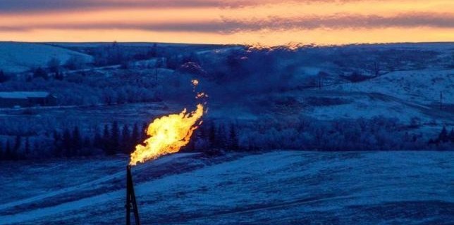 A natural gas flare on an oil well pad burns as the sun sets outside Watford City, North Dakota