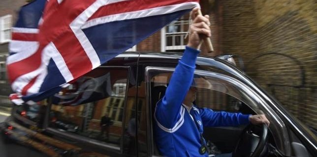 A taxi driver holds a Union flag, as he celebrates following the result of the EU referendum, in central London