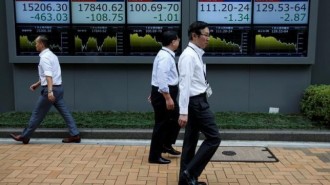 A man stands next to an electronic board showing stock prices in Tokyo