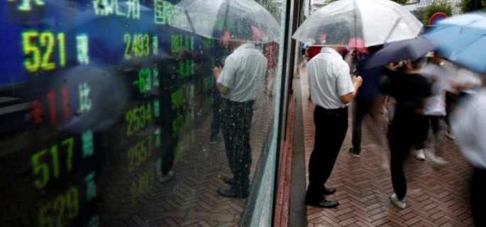 A man stands next to an electronic board showing stock prices in Tokyo