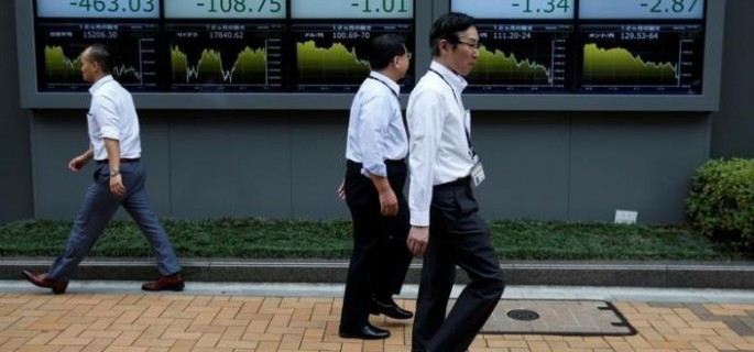 Passersby walk past in front of electronic boards showing Japan's Nikkei share average, the Japanese yen's exchange rate against the U.S. dollar, British pound and Euro outside a brokerage in Tokyo, Japan