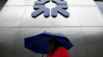 A woman shelters under an umbrella as she walks past a branch of RBS in the City of London