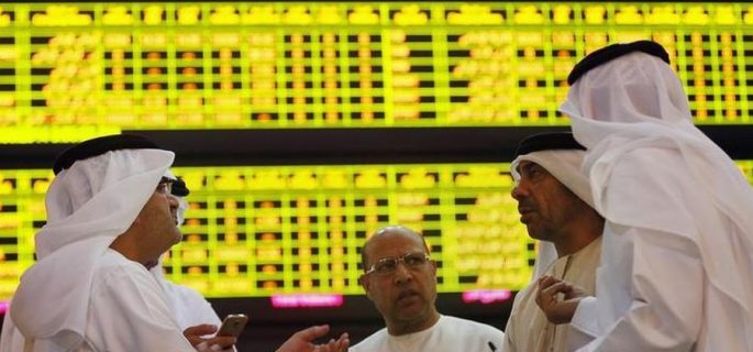 Investors speak in front of a screen displaying stock information at the Abu Dhabi Securities Exchange